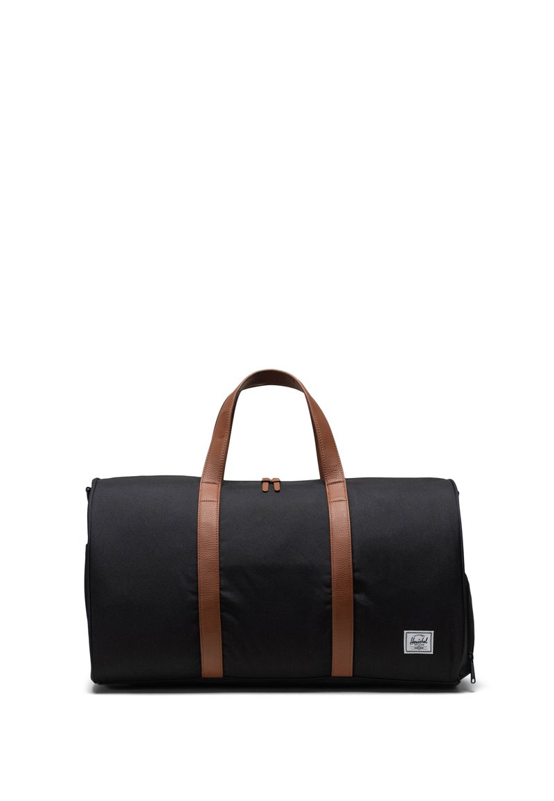 Sort duffel taske med to brune læderhåndtag, rektangulær form, tekstureret stof og et lille mærke på forsiden.
