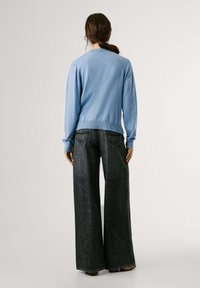 Šviesiai mėlynas megztinis su ilgomis rankovėmis, su gilioje kaklo linijoje ir juosmens kraštu. Derinamas su tamsiomis plačiomis džinsų kelnėmis, turinčiomis užpakalines kišenes ir siuvinėjimo detalėmis.