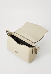 Beige skinnveske med teksturert overflate, rektangulær form og klaffelukking. Har svart innside og en justerbar stropp.
