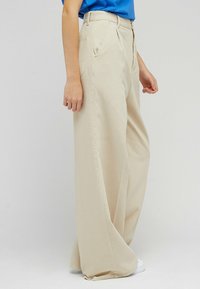 Beżowe spodnie wide-leg wykonane z tkaniny bawełnianej, z przednimi kieszeniami, wysokim stanem i gładką strukturą.