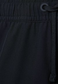 Pantaloni sportivi neri con una texture liscia, cintura elastica e un cordoncino con una estremità in plastica. La cucitura crea un motivo sottile.