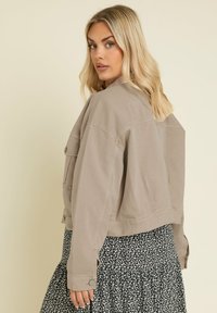 Avklippt beige denimjacka med knäppta fickor och långa ärmar, bärs över en svart blommönstrad kjol.