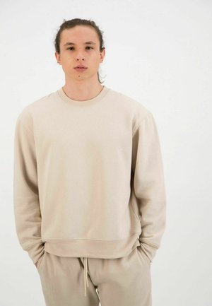 Beige sweatshirt with a crew neck and long sleeves, made of soft fabric. Features a relaxed fit and ribbed cuffs, worn with matching pants.