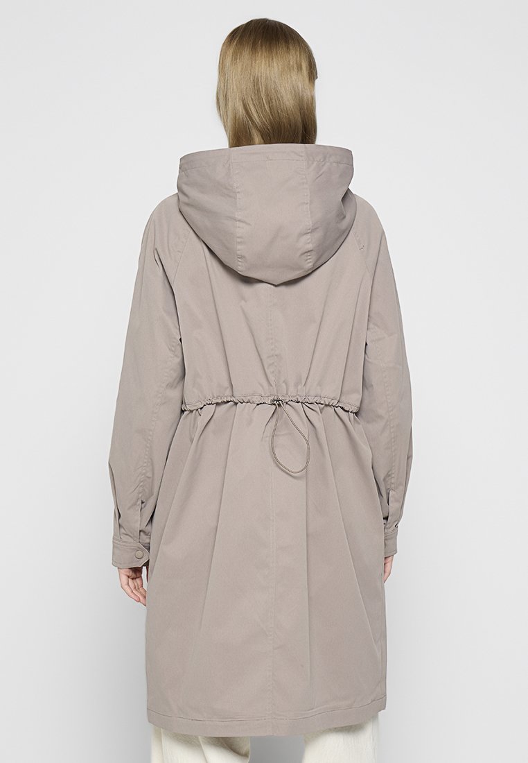 Manteau long beige avec une capuche, taille à cordon de serrage et poignets boutonnés. Texture lisse, design simple et coupe mi-longue.