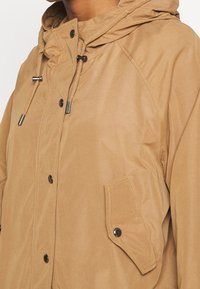 Brown hooded jacket made of a smooth, matte fabric. Features a front snap closure and a pocket with a rounded flap. Adjustable drawstrings at the hood.