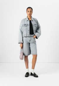 Ljust grå denimjacka och shorts, svart topp, vita strumpor, svarta loafers och en liten rosa väska. Enkelt design med synliga sömmar.