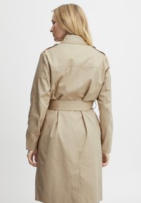 Beige Trenchcoat mit einem taillierten Gürtel, langen Ärmeln und Knopfakzenten. Der Stoff wirkt glatt mit einem dezenten Glanz. Die Rückansicht zeigt Faltendetails.