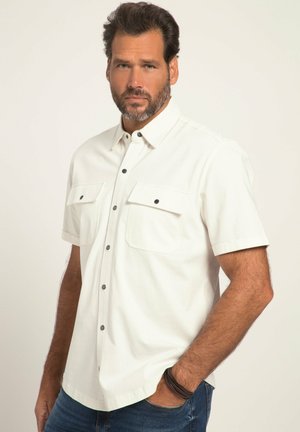 Camisa blanca de manga corta con dos bolsillos en el pecho, botones a presión negros y cuello abotonado. Tejido suave y corte ajustado.