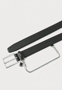 Ceinture en cuir noir avec une boucle à double ardillon en argent, détail en chaîne et charm amovible. Texture lisse avec des trous uniformément espacés.