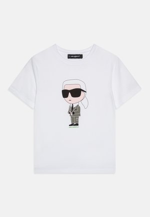 T-shirt en coton blanc avec une illustration de dessin animé représentant une personne portant des lunettes de soleil noires et un vêtement gris, avec "Karl Lagerfeld" imprimé en vert.