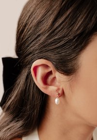 Złote kolczyki na sztyfcie z białą perłą, z kulistym akcentem nad perłą i gładkim, wypolerowanym wykończeniem.