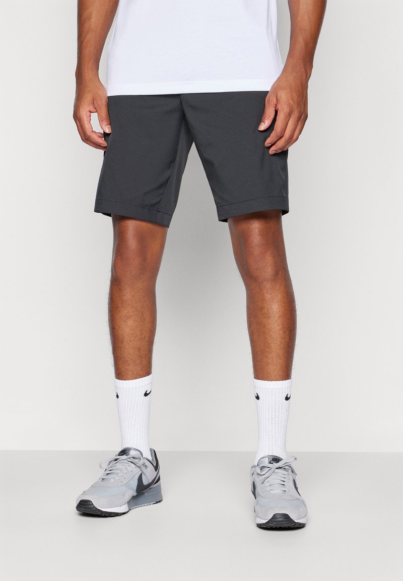 Calções atléticos cinza-escuro com uma textura suave, bainha dobrada e um corte regular, combinados com ténis cinza e meias brancas da Nike.