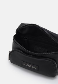 Svart läder kosmetikväska med en texturerad yta, dragkedjeöppning och innerficka. Har en märkesetikett inuti.