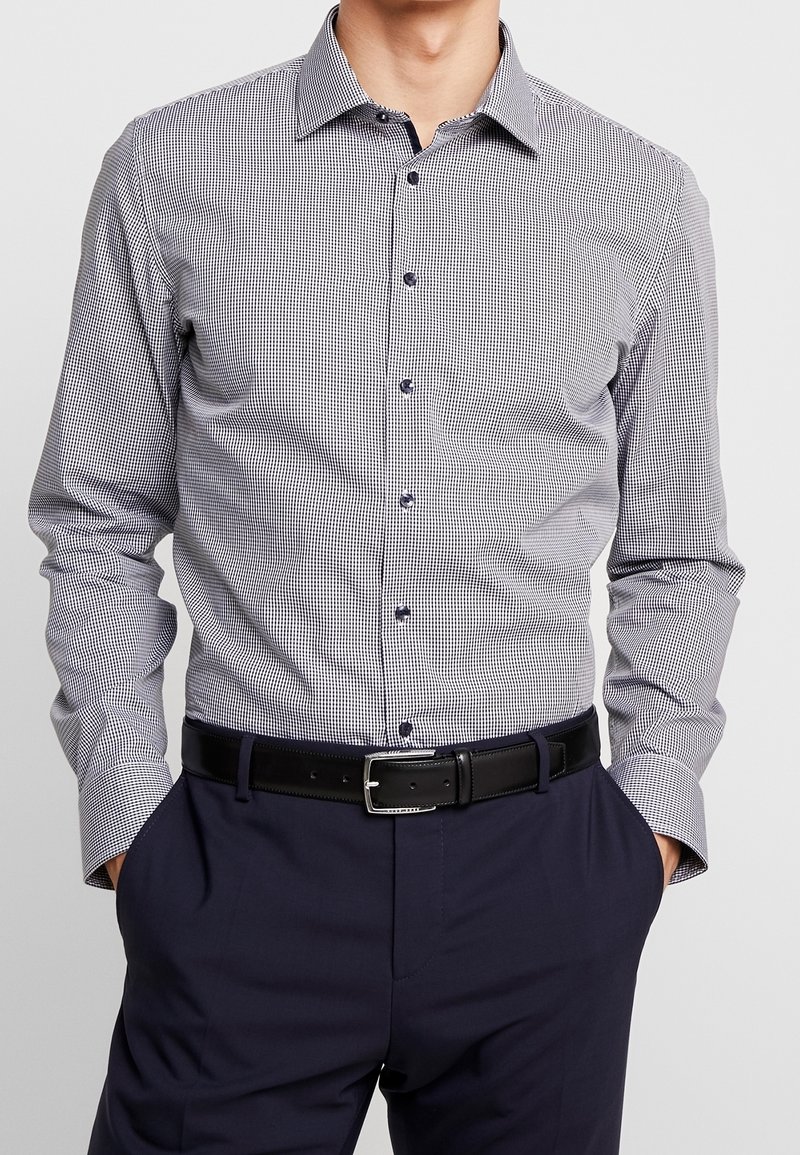 Randig skjorta i marinblått och vitt, med krage som knäpps, långa ärmar och en smal passform. Matchad med ett svart bälte.