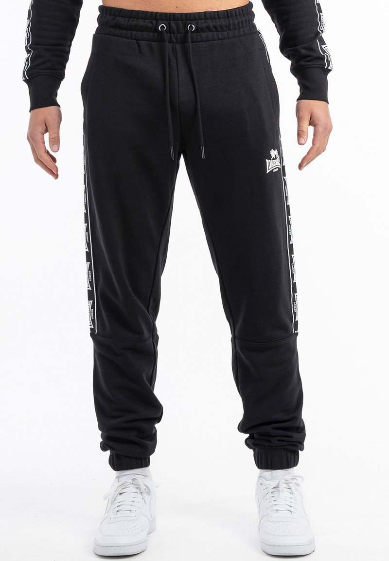 Pantalones de chándal negros con cintura ajustable, bolsillos laterales y acentos de logo blanco a lo largo de las costuras exteriores. Tobillos ajustados para un ajuste ceñido.