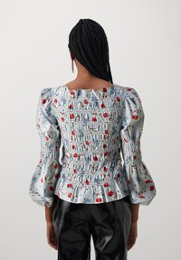 Top floreale smockato con righe blu e bianche, fiori rossi e blu, maniche a sbuffo e scollatura quadrata, abbinato a pantaloni in vernice nera.