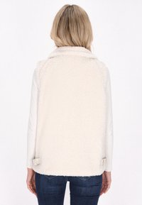 Faux-Fur-Weste in Cremefarbe mit kragenförmigem Ausschnitt und verstellbaren Seitenriemen. Weiche Textur mit flauschiger Oberfläche.