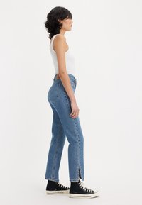 Light-wash denim jeans with a straight fit, mid-rise waist, and side slit detailing, paired with black high-top sneakers.