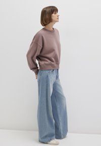 Oversized mauve sweatshirt with ribbed cuffs and hem paired with high-waisted light blue wide-leg jeans. Neutral-toned footwear visible.