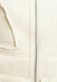 Kremowa bluza z polaru z pełnym zamkiem błyskawicznym, miękką, teksturowaną powierzchnią oraz futrzanym obszyciem przy kołnierzu i dolnym brzegu.