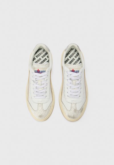 White sneakers with cracked metallic silver accents, flat white laces, and a textured cream rubber sole. Interior features branded black text.