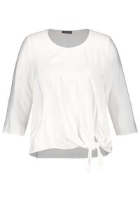Blouse blanche à manches longues avec encolure ronde et détail de nouage sur le côté, tissu légèrement texturé, et coupe décontractée.