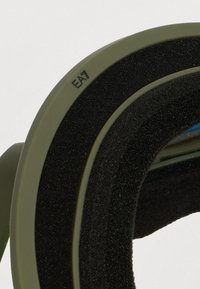 Κοντινό πλάνο μαξιλαριού ακουστικών σε ελιά πράσινου χρώματος με μαύρο αφρώδες επένδυση και σήμανση "EA7" στην εξωτερική άκρη.