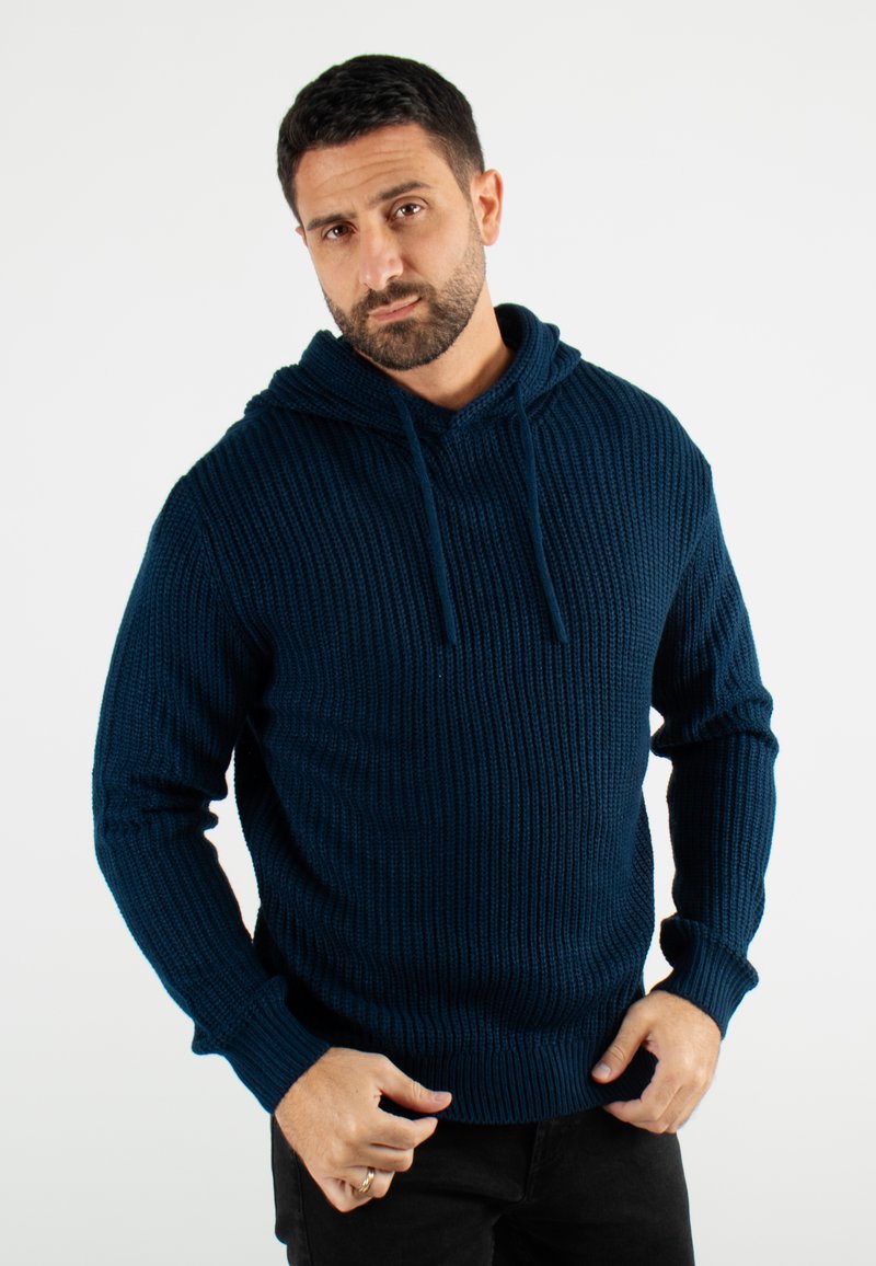 Hoodie tricoté bleu marine avec texture côtelée, capuche à cordon et manches longues. Le modèle le porte avec un pantalon noir sur un fond blanc.