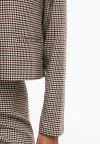 Detailní záběr na sako a sukni na míru s malým vzorem psí zub v černé, bílé a červené barvě.