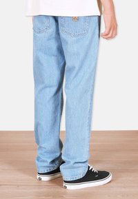 Vaaleansiniset farkut, joissa on suora lahje, haalistunut pinta, takataskut ompelutiedoilla ja näkyvä logopatch.