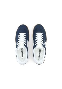 Baskets en daim bleu marine avec des lacets blancs, des accents latéraux blancs et des semelles en caoutchouc marron. L'intérieur présente un texte de marque en noir.