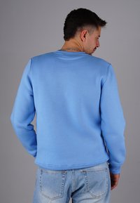 Blaues Sweatshirt aus weichem Stoff mit Rundhalsausschnitt und gerippten Bündchen, kombiniert mit hellblauen Jeans. Einfaches, lässiges Design.
