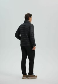 Black puffer jacket with horizontal baffles, high collar, and long sleeves, paired with black pants and beige hiking shoes.