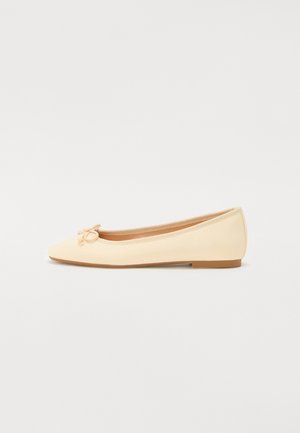 Vaaleankeltaiset balettikengät, joissa on kärjestä kapeneva muoto, pehmeä kangaspinta ja pieni nauha etuosassa. Litteä pohja helppoa käyttöä varten.