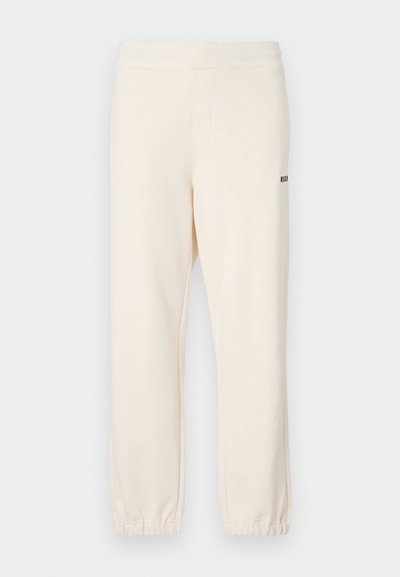 Cream-colored jogger pants with elastic waistband and cuffs, featuring side pockets and a small black logo on the back.