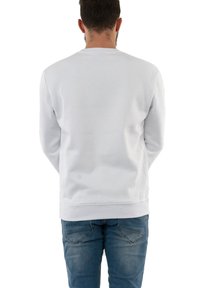 Witte sweatshirt met ribgebreide manchetten en zoom, met een gladde textuur. Draagt met blauwe spijkerbroek, weergegeven vanuit de achterkant.