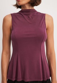 Bordowy bezrękawnik z wysokim dekoltem, wykonany z gładkiego materiału. Posiada rozszerzaną linię dołu i starannie wykończone szwy.