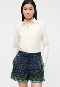 Camisa branca com colarinho usada com calções azul-marinho com bolinhas brancas, uma borda padrão, cintura elástica e bolsos laterais.