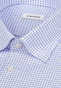 Chemise à carreaux bleu clair et blanc avec col boutonné et étiquette de marque « seidensticker » à l'intérieur du col.