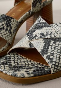 Sandali con stampa serpente in bianco e nero, caratterizzati da un design con parte superiore incrociata e tacco in legno. Materiale strutturato con una soletta liscia color tan.