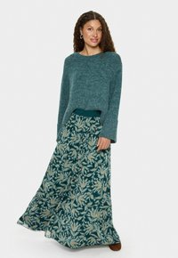 Teal strikpullover med lange ærmer, parret med en flydende, mønstret maxi-nederdel med grønne, gyldne og orange blomsterdesigns.