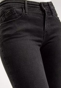 Czarne dżinsy o dopasowanym kroju, z kieszenią z przodu, szlufkami na pasek oraz subtelnymi detalami przeszycia. Gładka tekstura i klasyczny styl.
