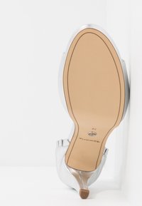 Chaussure à talon haut argentée reposant sur son bout, montrant une semelle beige avec la pointure 38 et la marque "Tamaris".