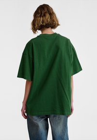Green oversized t-shirt made of cotton, featuring a round neckline and short sleeves. The back is plain with no visible logos or patterns.