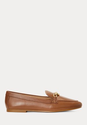 Naisten ruskea nahkainen slip-on-loafer, jossa kultainen metallinen koriste ja litteä pohja, esitetty sivuprofiilissa valkoisella taustalla.