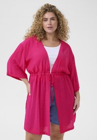 Vaaleanpunainen kimono-tyylinen peite, kevyt kangas, V-pääntie, nyöri vyötäröllä, lyhyet hihat ja sivuaukot liikkumisen helpottamiseksi.