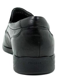Zapato negro de cuero sin cordones con punta redondeada, textura suave y suela de goma contrastante, con detalles de costura sutiles.