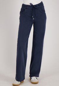Marineblauwe casual broek met een trekkoord in de taille en voorzakken, gedragen met witte sneakers met zwarte strepen.