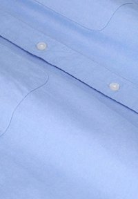 Lichtblauw katoenen shirt met een gladde textuur, zichtbare stiksels en witte knopen langs de knoopsluiting. Eenvoudig ontwerp zonder patronen.