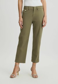 Pantaloni verde oliva con design a gamba dritta, tasche frontali e dettaglio con bottoni in vita, abbinati a tacchi a strappo con fantasia.